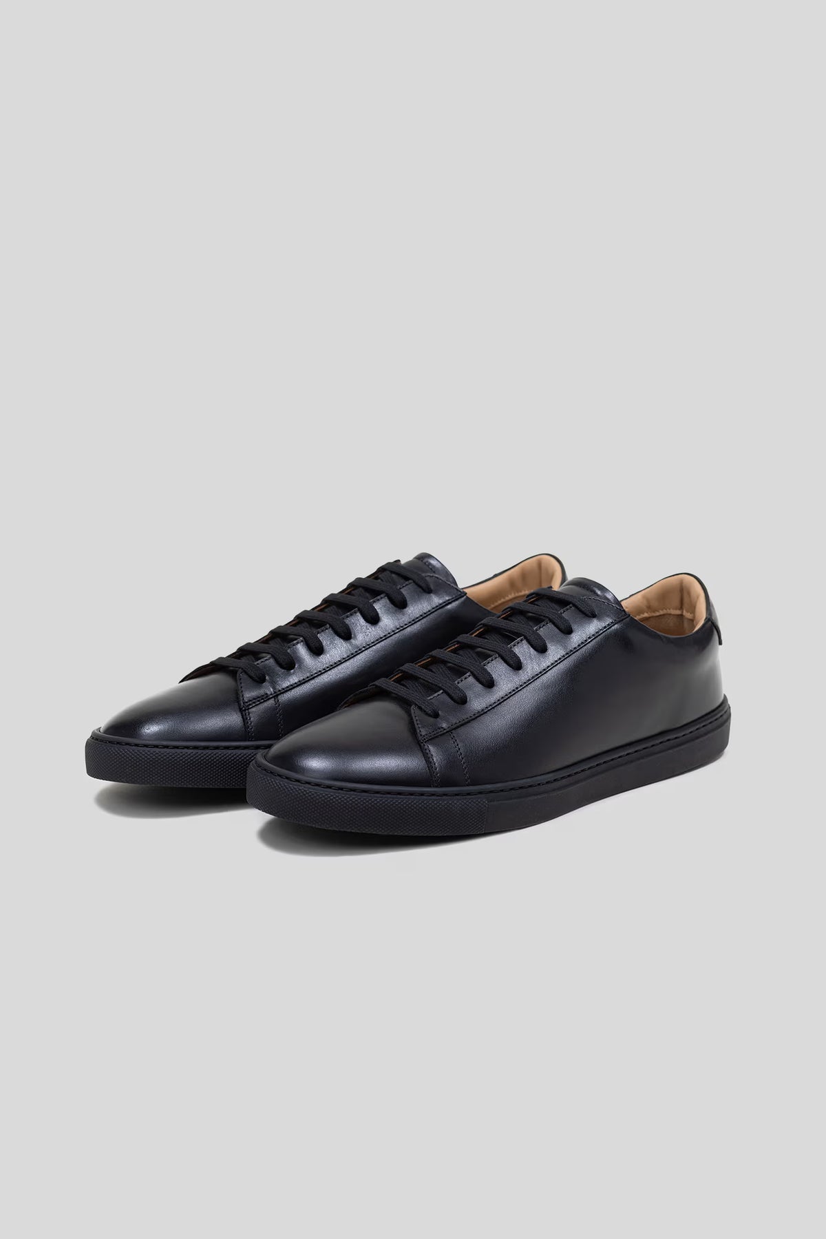 Three-quarter studio view of a pair of Olen Città low-top sneakers in black calfskin leather with neutral tan lining.