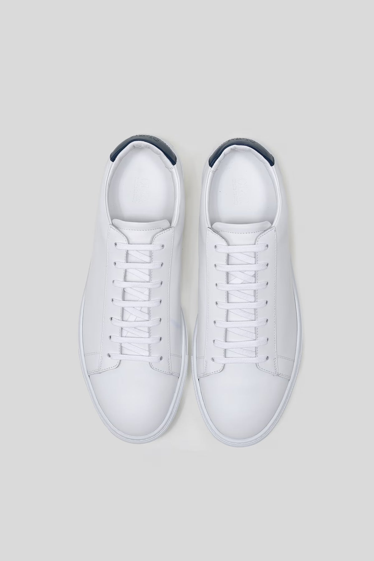 Top-down studio view of a pair of Olen Città low-top sneakers in white calfskin leather with navy heel tabs.