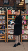Man wearing a black coat and black calfskin Olen Città sneakers reading a book outside a bookstore window display.