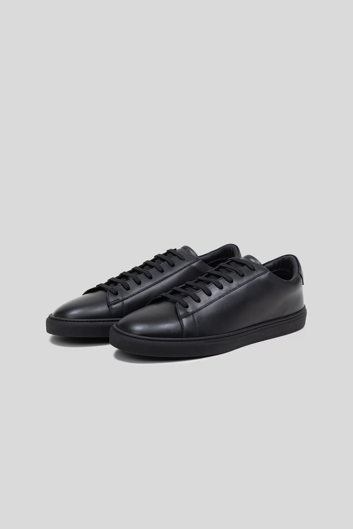 Three-quarter studio view of a pair of Olen Città low-top sneakers in black calfskin leather.