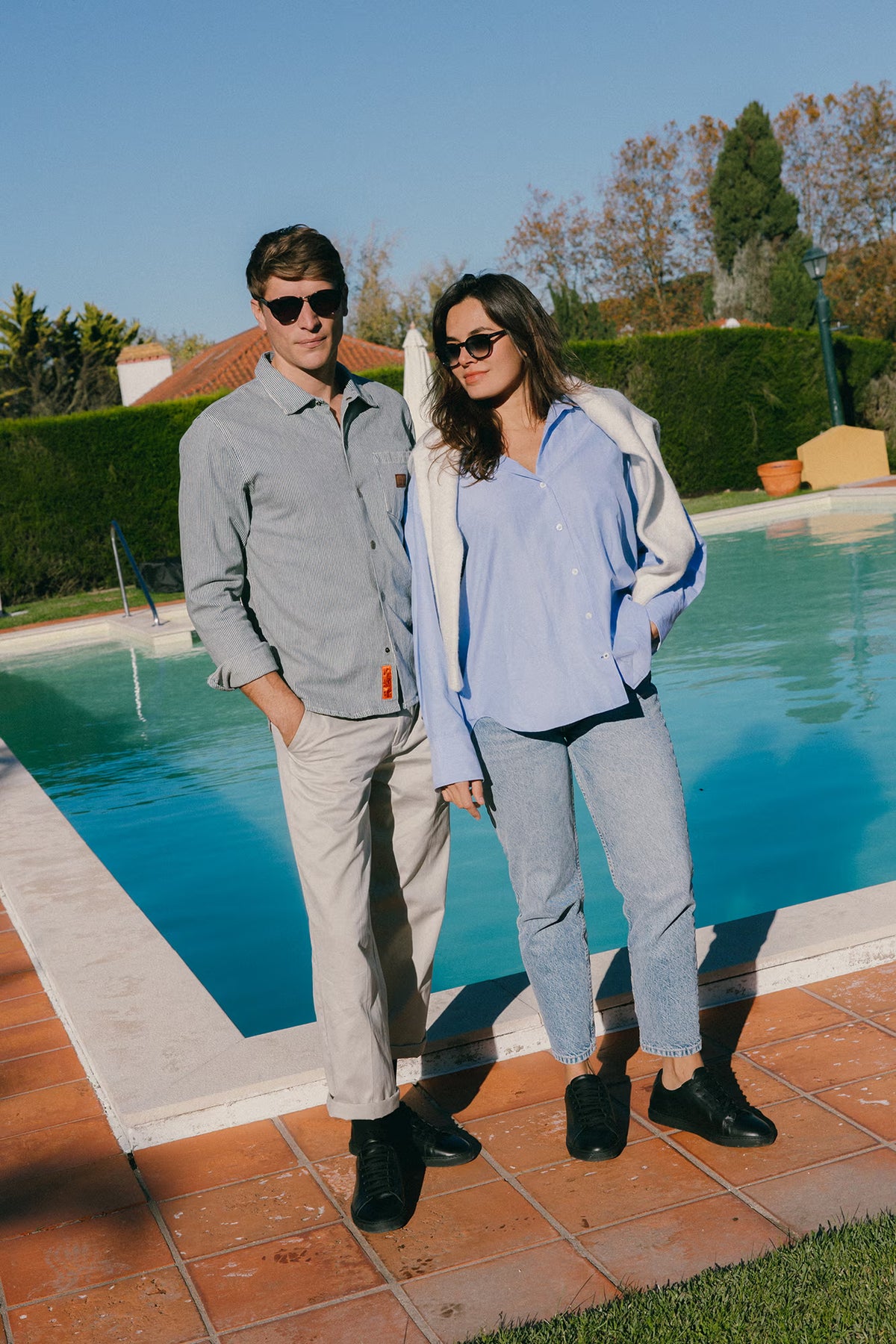 Full-length poolside lifestyle shot of a couple wearing black calfskin Olen Città sneakers with casual resort outfits.