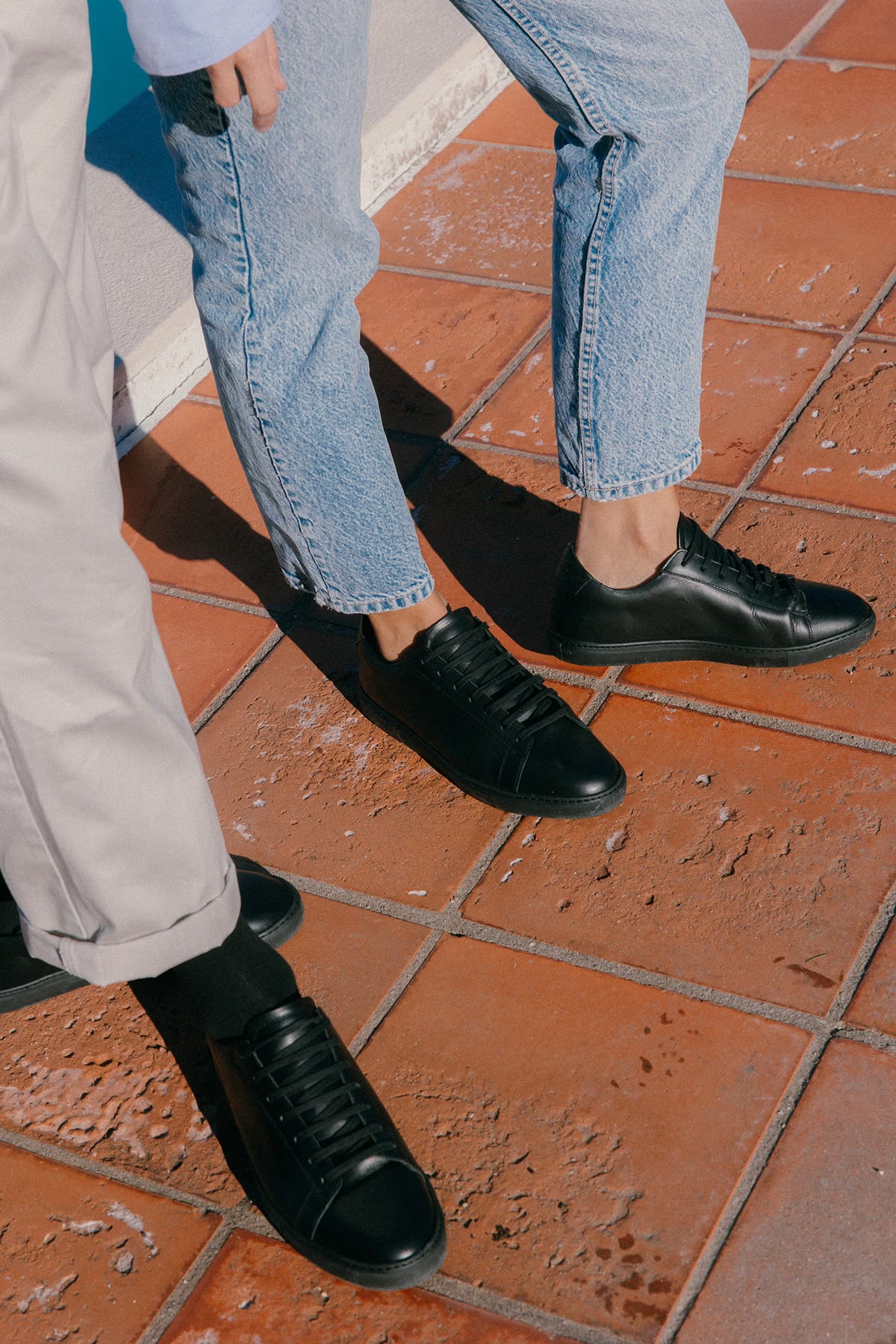 Close-up view of black calfskin Olen Città sneakers worn on terracotta tile with light denim jeans and beige trousers.