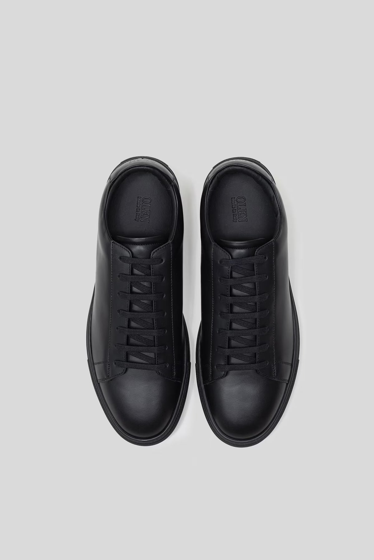 Top-down studio view of a pair of Olen Città low-top sneakers in black calfskin leather.