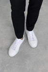 Overhead top-down view of a pair of Olen Città sneakers in off-white calfskin leather on-foot with dark trousers.