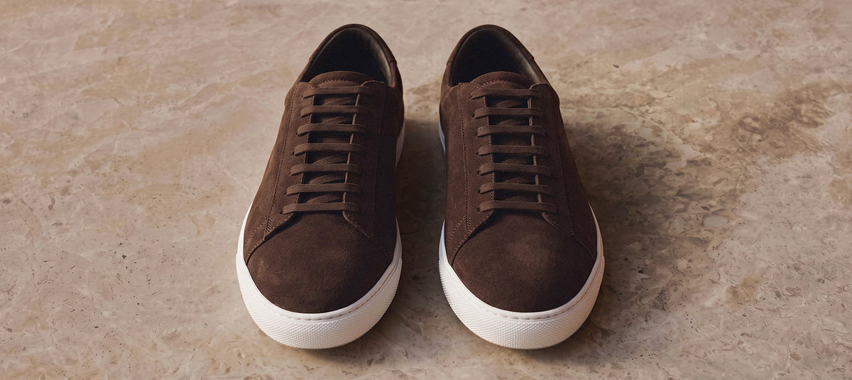 Dark brown suede Città sneakers with white soles on a beige stone background by Olen.