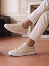 Beige leather sneakers styled with cream trousers in an elegant European interior, showcasing a clean minimalist design.