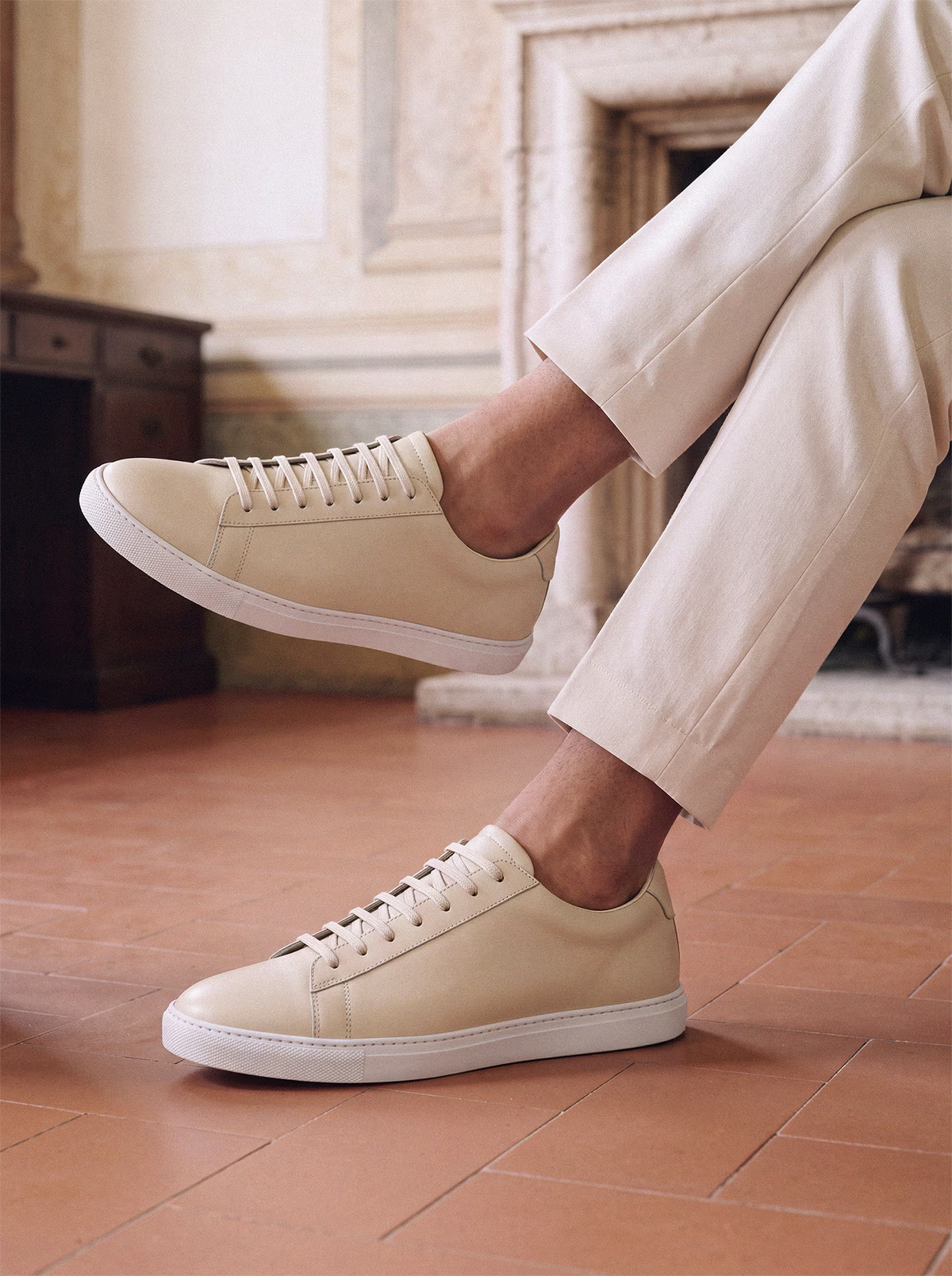 Beige leather sneakers styled with cream trousers in an elegant European interior, showcasing a clean minimalist design.