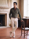 Man wearing cream Italian leather sneakers with tailored trousers and a dark green shirt in an elegant European interior
