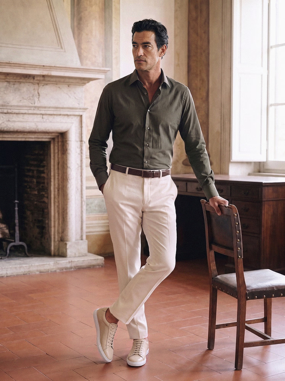 Man wearing cream Italian leather sneakers with tailored trousers and a dark green shirt in an elegant European interior